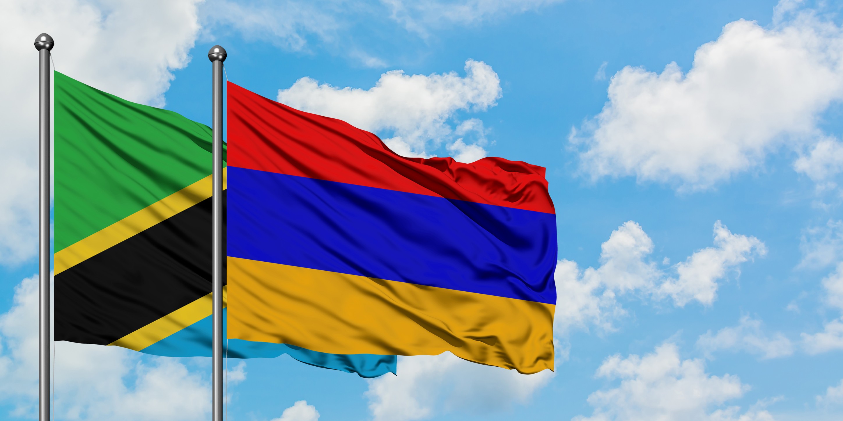 Flags Of Tanzania And Armenia Waving In The Wind Against A Cloudy Blue Sky