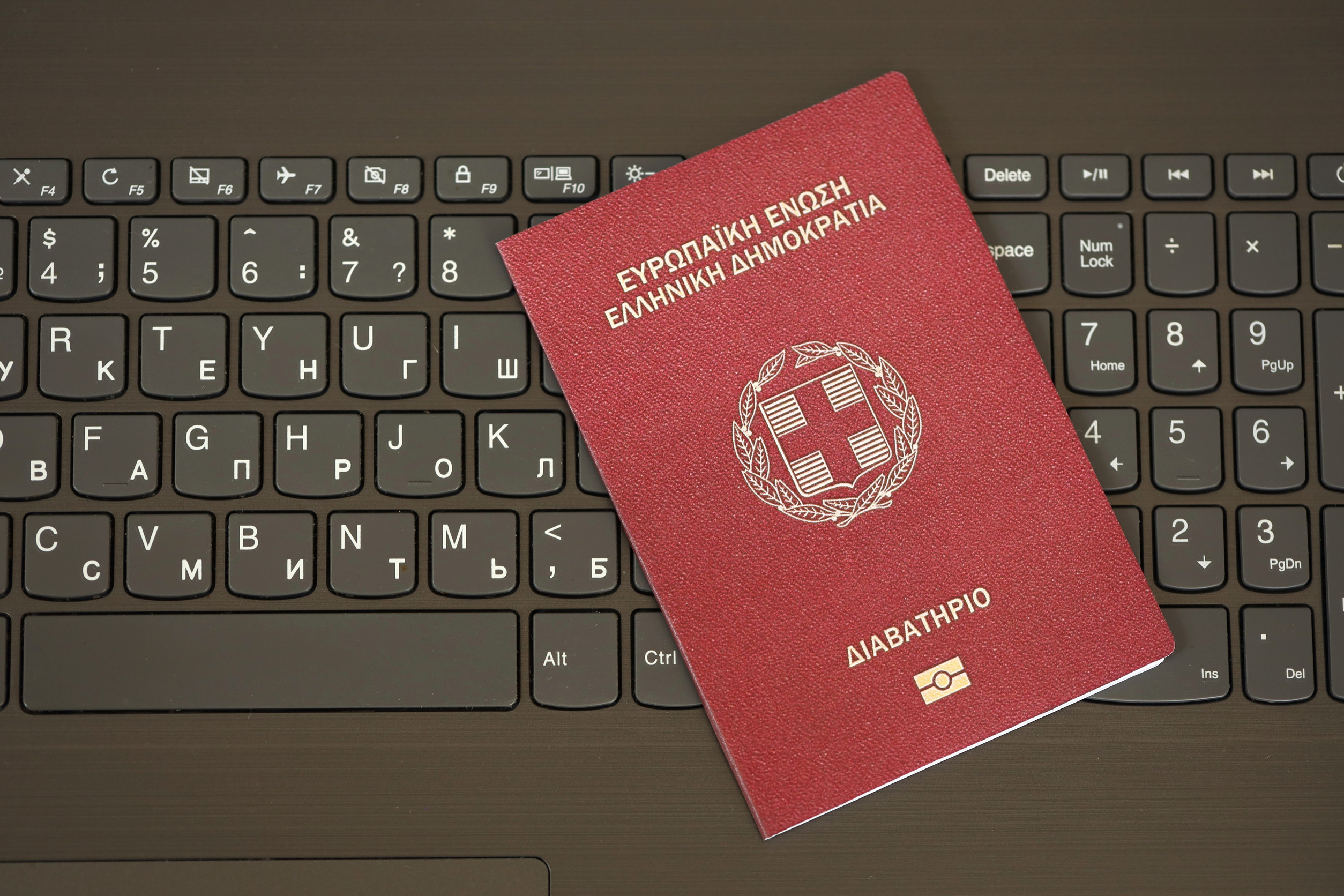 Greece Passport Lies On Black Laptop