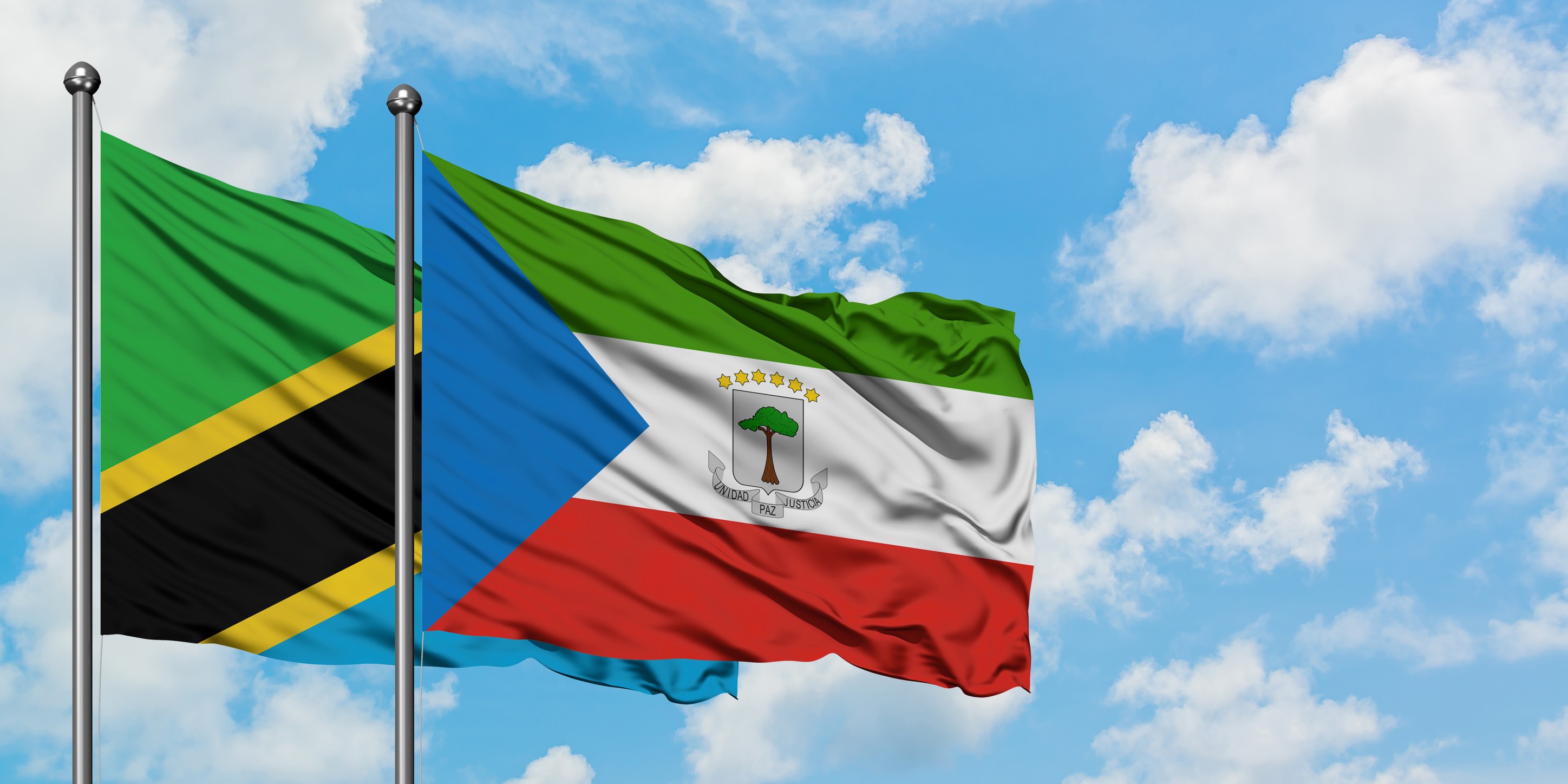 Tanzania And Equatorial Guinea Flag Waving In The Wind Against White Cloudy 